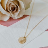 Lat & Lo disc necklace in 14K gold filled, with custom back inscription laying flat with rose.