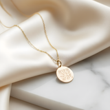 Gold necklace with a round pendant featuring a QR code on a beige fabric background