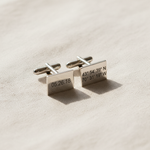 Silver cufflinks with engraved text on a beige fabric background