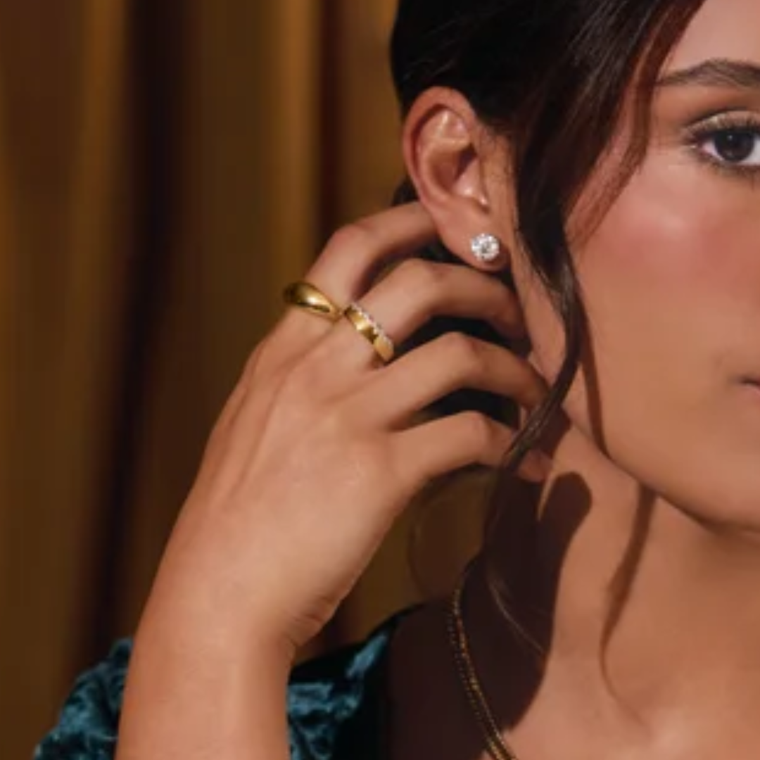 Close-up of a woman wearing gold earrings and a gold ring, with a blurred background.