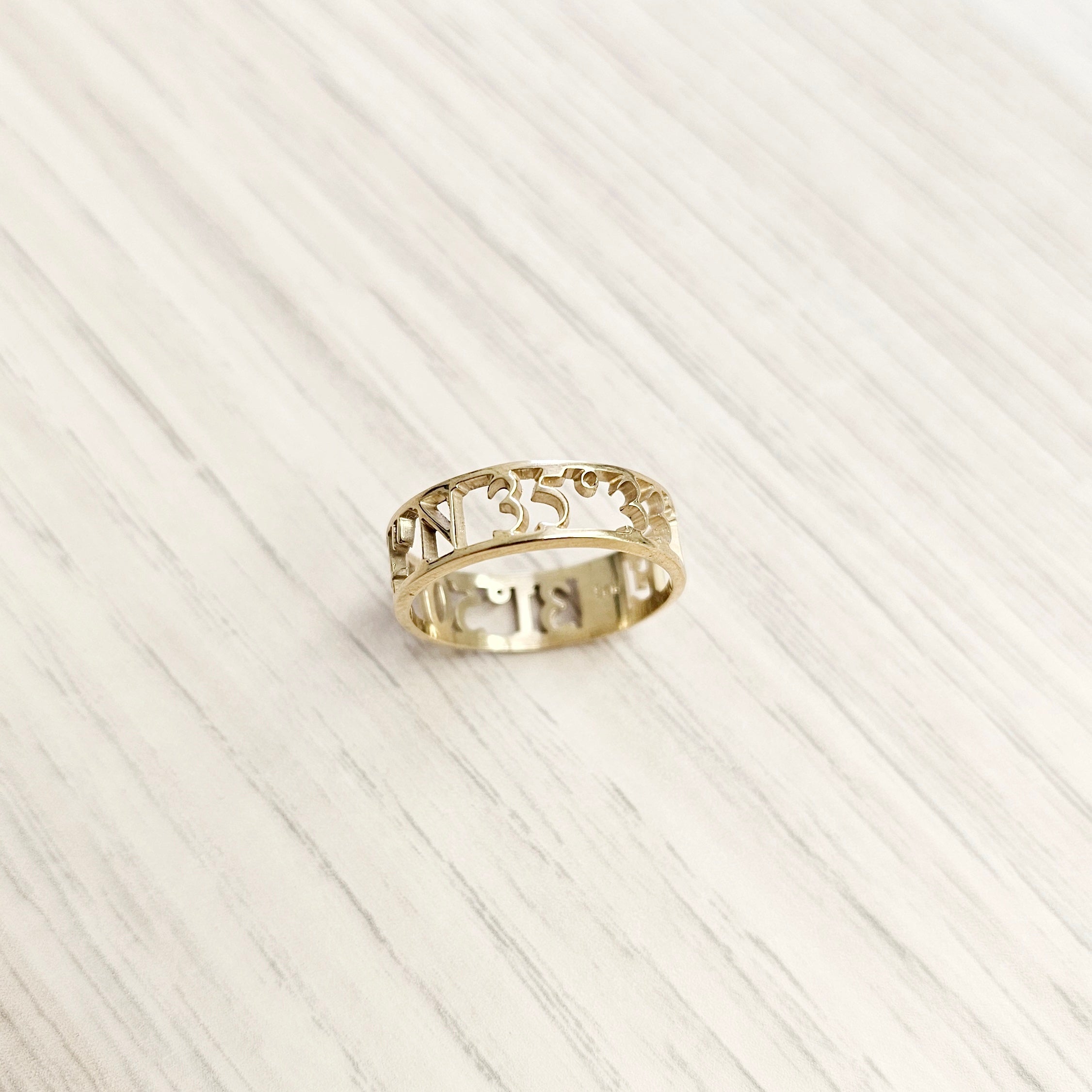 gold cut-out-style coordinates ring on table top view-lat & lo personalized jewlery collection