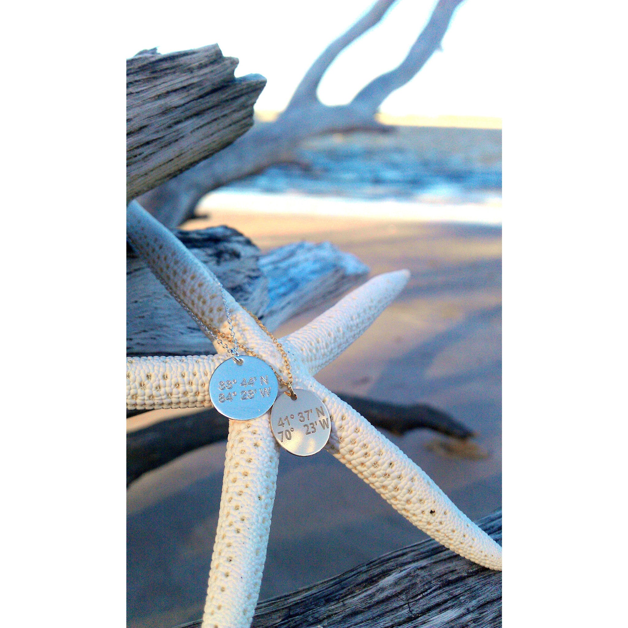 Lat & Lo disc necklace custom inscribed with coordinates hanging on a star fish on the beach.