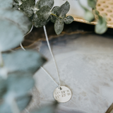 Lat & Lo Disc necklace inscribed with coordinates in sterling silver, laying flat around greenery.