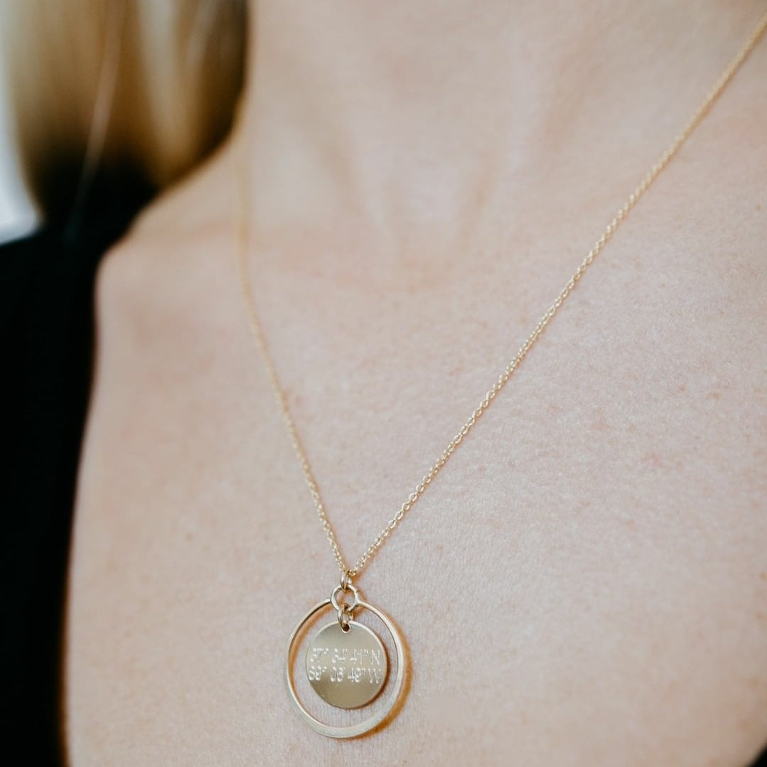 Lat & Lo eclipse necklace, inscribed with coordinates, 14K gold filled, 13mm charm with halo ring surrounding, on figure